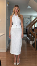 Front view of woman wearing white sleeveless peplum top and white midi skirt set