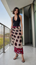 Front view of woman wearing beige polka dot wrap maxi skirt and black halter top