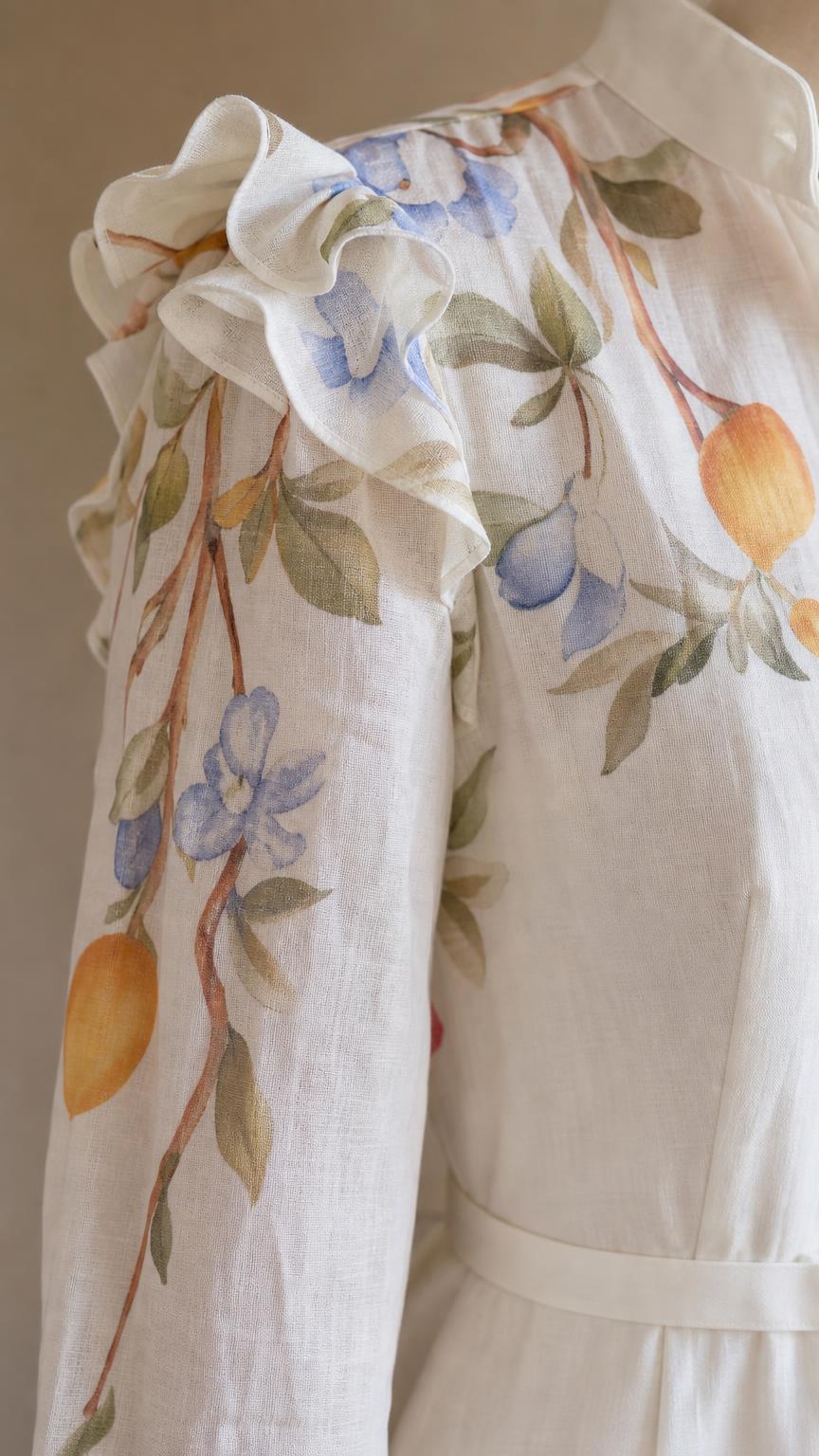 Close-up of shoulder ruffles and botanical embroidery on white fabric