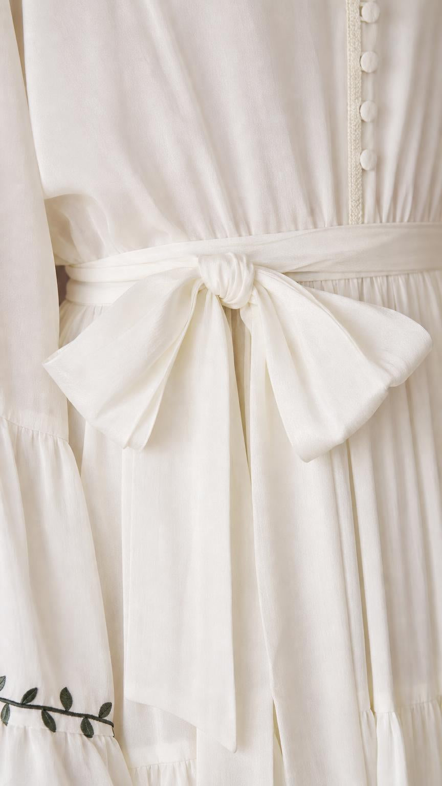 Close-up of the ivory dress tie waist, gathered fabric, buttons, and decorative sleeve trim