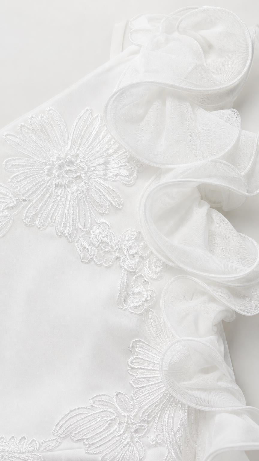 Close-up detail of fabric, ruffles, and floral embroidery