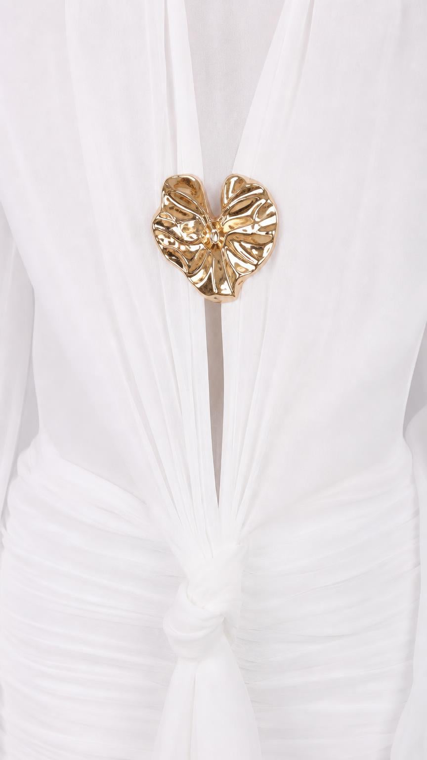 Close-up of gold-toned sculptural hardware on white dress